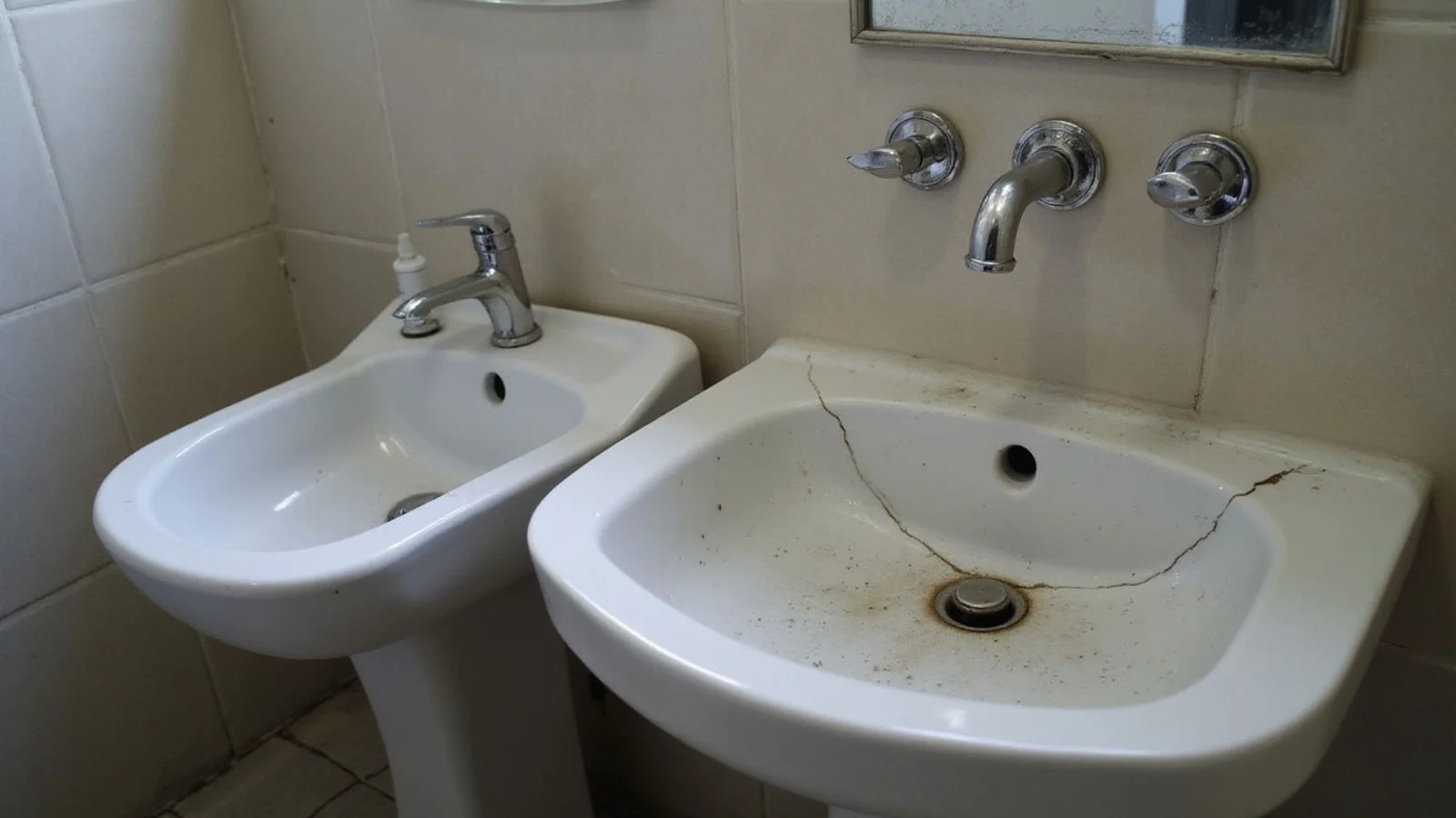 Old cracked sink beside a new washbasin
